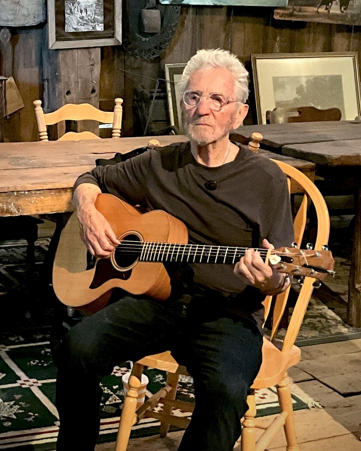 Don Stevenson seated in a wooden barn, playing an acoustic guitar